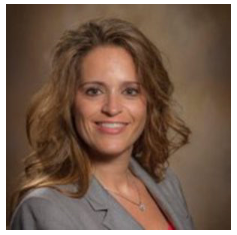 A woman with wavy brown hair wearing a gray blazer and red top, smiling at the camera against a brown background, representing Outpatient Therapy in Minnesota with St. Francis Health Services.