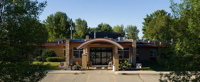 A single-story brick building with a large arched entrance, surrounded by trees and a parking area in front. A single-story brick building with a large arched entrance, surrounded by trees and a parking area in front.