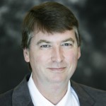 A man with short brown hair wearing a gray suit jacket and white collared shirt poses in front of a blurred dark background, representing St. Francis Health Services and its Outpatient Therapy in Minnesota. A man with short brown hair wearing a gray suit jacket and white collared shirt poses in front of a blurred dark background, representing St. Francis Health Services and its Outpatient Therapy in Minnesota.