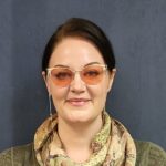 Woman with dark hair wearing orange-tinted glasses, a patterned scarf, and a green top stands in front of a plain dark blue background, reflecting the welcoming spirit of St. Francis Outpatient Therapy. Woman with dark hair wearing orange-tinted glasses, a patterned scarf, and a green top stands in front of a plain dark blue background, reflecting the welcoming spirit of St. Francis Outpatient Therapy.
