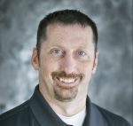 Man with short brown hair, light skin, and a trimmed goatee wearing a dark collared shirt, smiling at the camera with a blurred gray background, representing St. Francis Health Services in Minnesota. Man with short brown hair, light skin, and a trimmed goatee wearing a dark collared shirt, smiling at the camera with a blurred gray background, representing St. Francis Health Services in Minnesota.