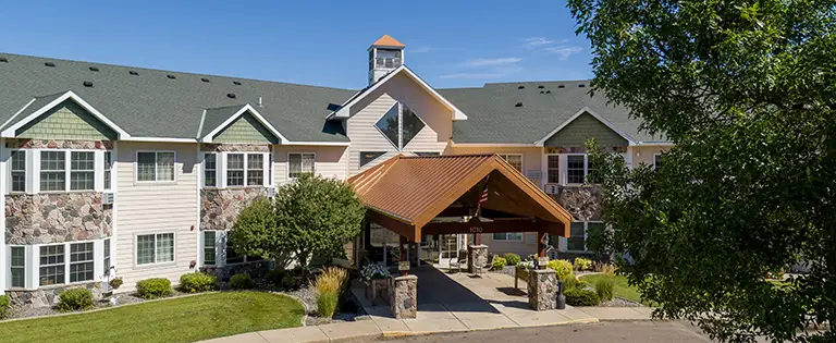 Two-story building with a green roof and stone accents, featuring a covered entryway, surrounded by trees and landscaping under a clear blue sky. Two-story building with a green roof and stone accents, featuring a covered entryway, surrounded by trees and landscaping under a clear blue sky.