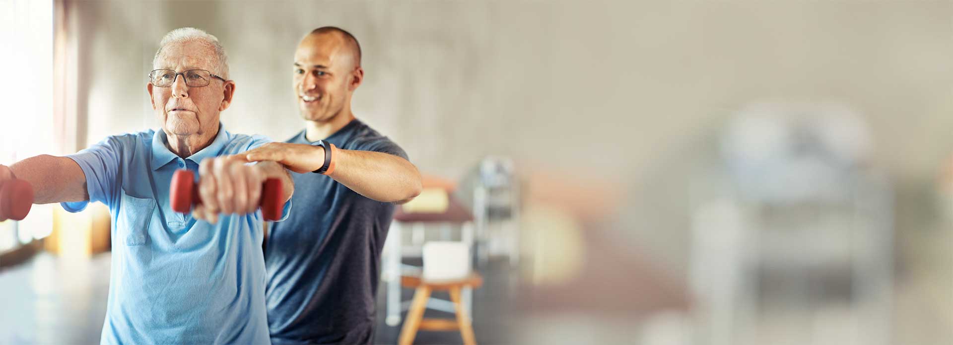 An elderly man lifts small dumbbells with guidance from a younger male trainer in a brightly lit room, showcasing St. Francis Health Services’ outpatient therapy in Minnesota. An elderly man lifts small dumbbells with guidance from a younger male trainer in a brightly lit room, showcasing St. Francis Health Services’ outpatient therapy in Minnesota.