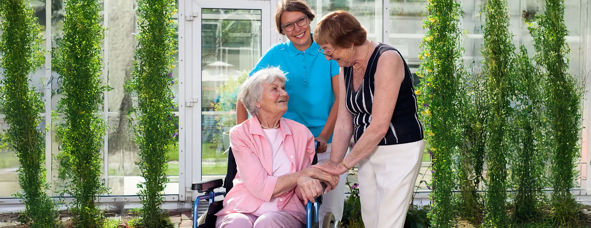 Three people are outside a white building at St. Francis Outpatient Therapy in Minnesota; one woman sits in a wheelchair, another stands holding her hand, and a man stands behind them. All are smiling. Three people are outside a white building at St. Francis Outpatient Therapy in Minnesota; one woman sits in a wheelchair, another stands holding her hand, and a man stands behind them. All are smiling.