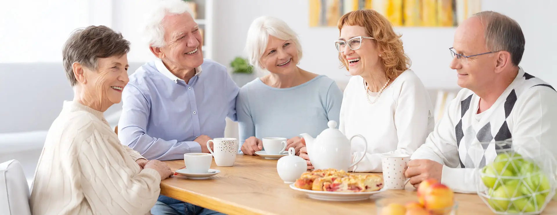 Five older adults sit around a table with tea, cups, and pastries, smiling and engaging in conversation at St. Francis Outpatient Therapy in Minnesota. Five older adults sit around a table with tea, cups, and pastries, smiling and engaging in conversation at St. Francis Outpatient Therapy in Minnesota.