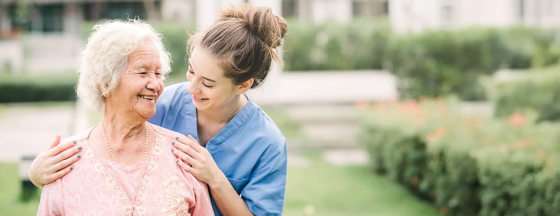 A young caregiver in blue scrubs stands outside with an elderly woman, smiling and placing her hands on the woman’s shoulders. Both appear happy and relaxed, reflecting the supportive approach of St. Francis Outpatient Therapy. A young caregiver in blue scrubs stands outside with an elderly woman, smiling and placing her hands on the woman's shoulders. Both appear happy and relaxed, reflecting the supportive approach of St. Francis Outpatient Therapy.