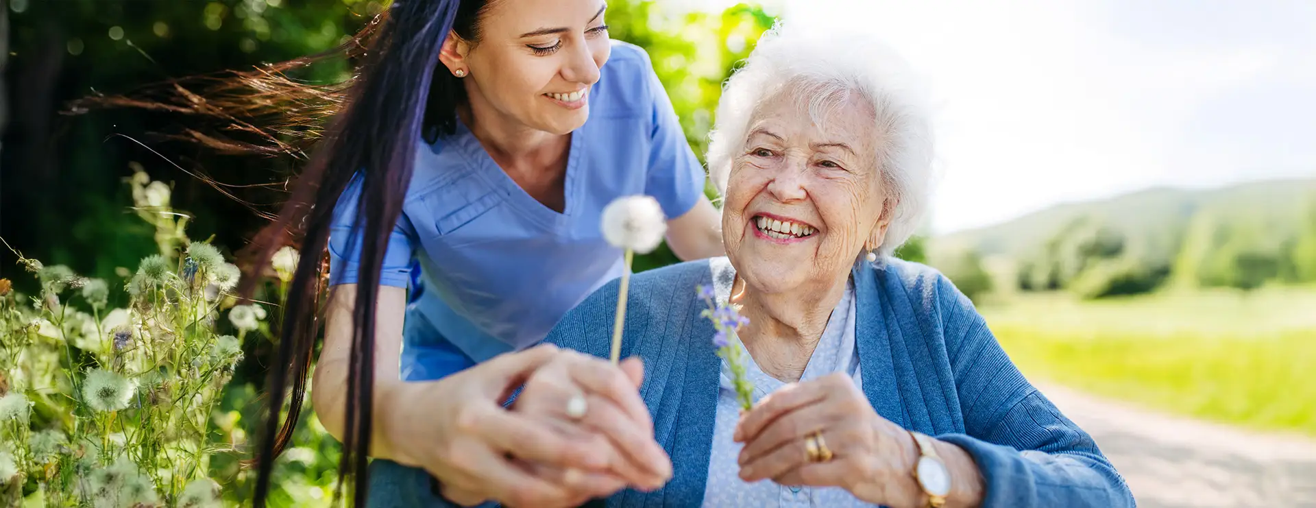 A young caregiver at Skyview Plaza helps an elderly woman hold flowers outdoors on a sunny day; both are smiling and enjoying the moment, capturing the warmth and companionship found in assisted living. A young caregiver at Skyview Plaza helps an elderly woman hold flowers outdoors on a sunny day; both are smiling and enjoying the moment, capturing the warmth and companionship found in assisted living.