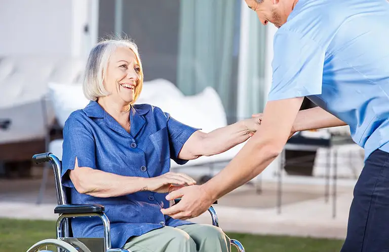 An elderly woman in a wheelchair smiles as a caregiver in blue scrubs from St. Francis Health Services assists her outdoors in Minnesota. An elderly woman in a wheelchair smiles as a caregiver in blue scrubs from St. Francis Health Services assists her outdoors in Minnesota.