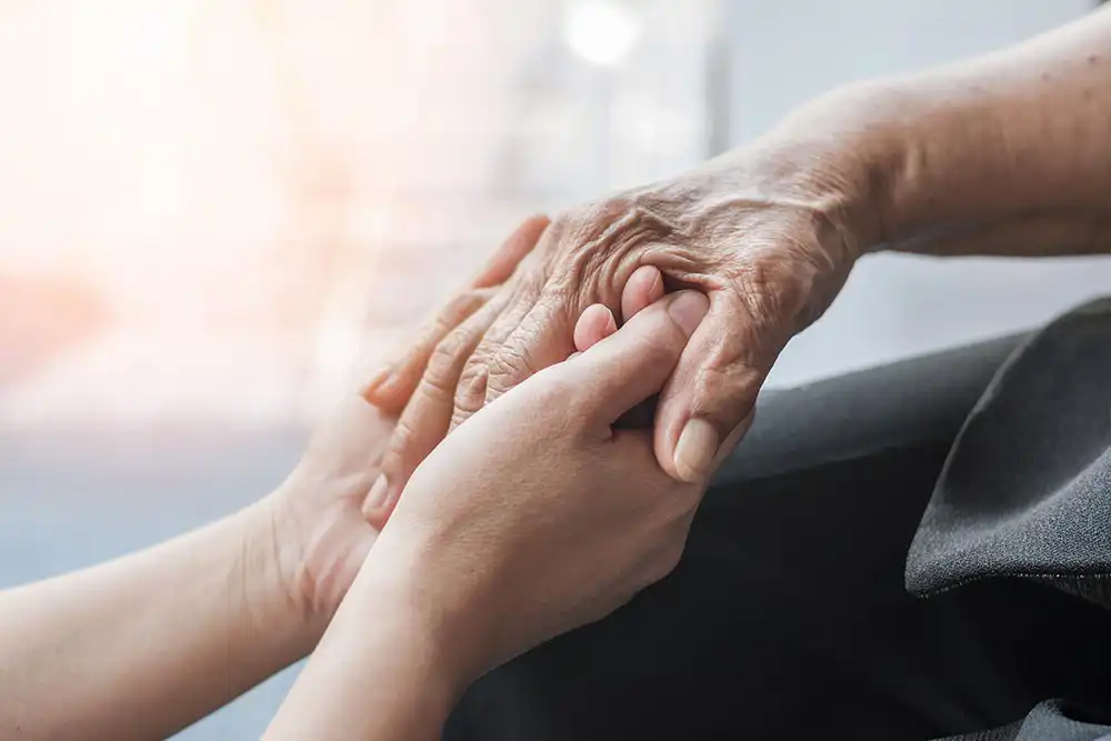 A younger person gently holding the hands of an older person, illustrating support and care.