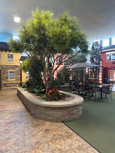 Indoor courtyard area with a large tree in a stone planter, surrounded by tables and chairs, and colorful buildings—offering a peaceful space at St. Francis Outpatient Therapy, part of St. Francis Health Services in Minnesota. Indoor courtyard area with a large tree in a stone planter, surrounded by tables and chairs, and colorful buildings—offering a peaceful space at St. Francis Outpatient Therapy, part of St. Francis Health Services in Minnesota.