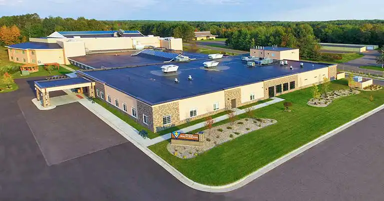 A large, single-story commercial building with a flat roof, surrounded by parking lots, landscaped areas, and trees in the background.