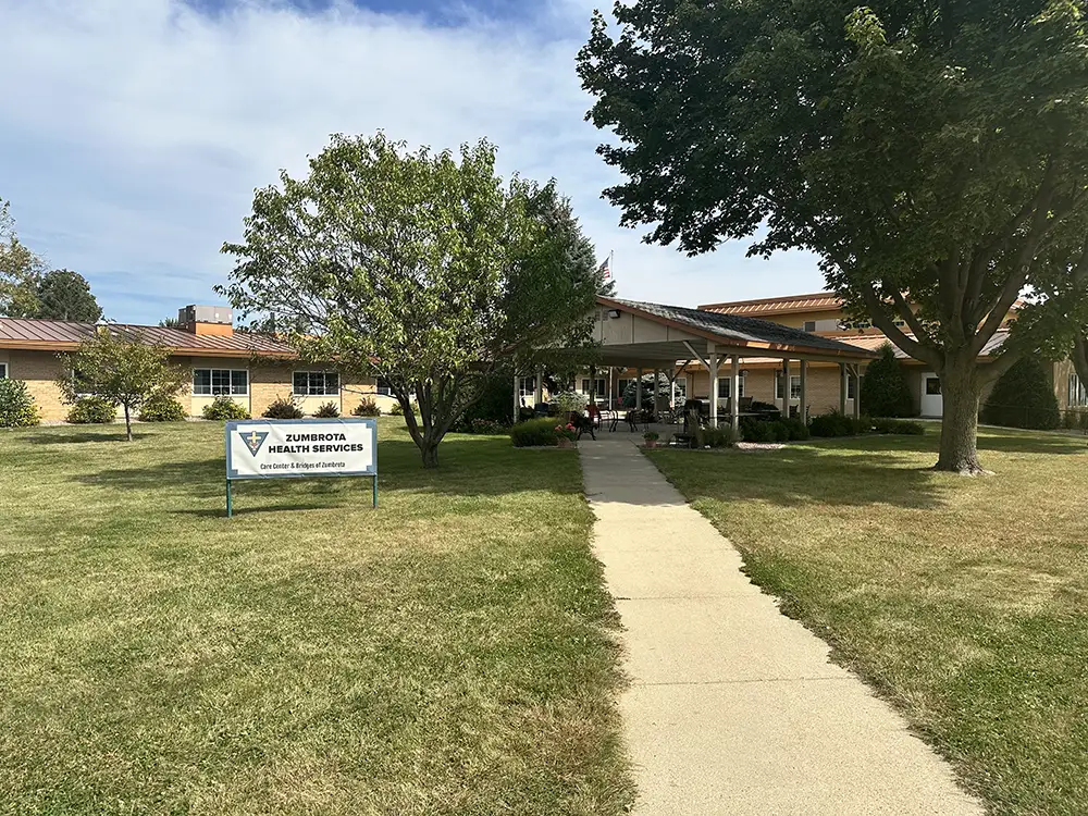A sidewalk leads to the entrance of a one-story building surrounded by trees and grass, with a sign reading “Sizihomora Health Services” on the lawn. A sidewalk leads to the entrance of a one-story building surrounded by trees and grass, with a sign reading "Sizihomora Health Services" on the lawn.