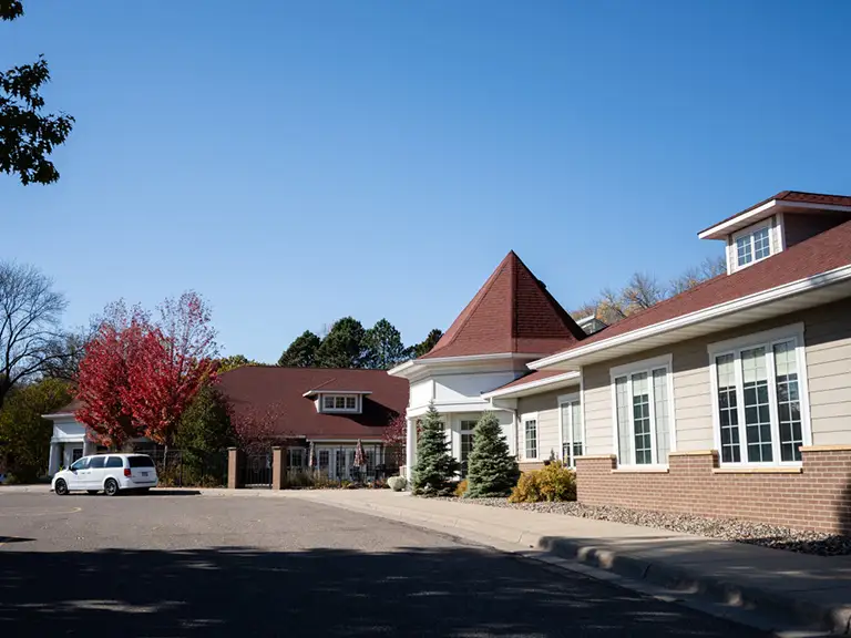 A white van is parked outside a building complex with brown roofs, white walls, and large windows under a clear blue sky. A white van is parked outside a building complex with brown roofs, white walls, and large windows under a clear blue sky.