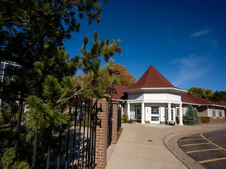 A white building with a red conical roof sits behind a brick fence and pine tree on a sunny day with a clear blue sky. A white building with a red conical roof sits behind a brick fence and pine tree on a sunny day with a clear blue sky.