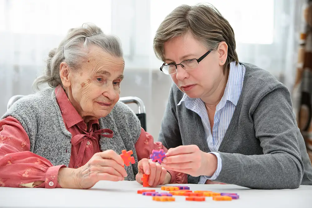 An elderly woman and a younger woman sit at a table assembling a colorful puzzle together, highlighting the supportive care offered by St. Francis Outpatient Therapy in Minnesota. An elderly woman and a younger woman sit at a table assembling a colorful puzzle together, highlighting the supportive care offered by St. Francis Outpatient Therapy in Minnesota.