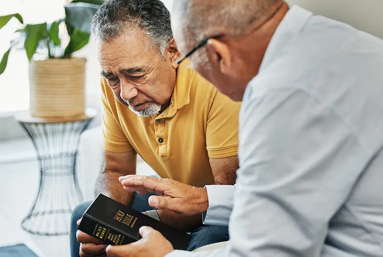 Two older men sit closely together indoors; one holds a book labeled “Holy Bible” while the other listens attentively with a serious expression, reflecting the supportive atmosphere found at St. Francis Outpatient Therapy in Minnesota. Two older men sit closely together indoors; one holds a book labeled "Holy Bible" while the other listens attentively with a serious expression, reflecting the supportive atmosphere found at St. Francis Outpatient Therapy in Minnesota.