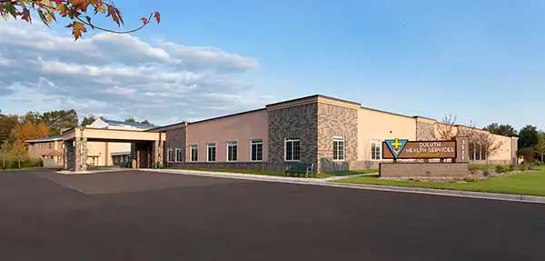 Single-story building with large windows, a covered entrance, and a sign reading “Duluth Health Services” on a landscaped lawn; clear sky in the background. Single-story building with large windows, a covered entrance, and a sign reading “Duluth Health Services” on a landscaped lawn; clear sky in the background.