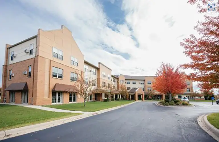 A three-story brick building with multiple windows and a driveway, surrounded by green grass and trees with autumn foliage. A three-story brick building with multiple windows and a driveway, surrounded by green grass and trees with autumn foliage.